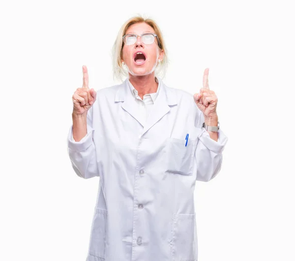 中年金发碧眼的治疗师妇女穿着白色外套在孤立的背景惊讶和惊讶地抬起头来 用手指和举起的手臂指指点点 — 图库照片