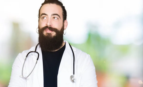 医療コートと見ている側と見つめて離れて思考を笑顔聴診器を身に着けている長い髪の医者 — ストック写真