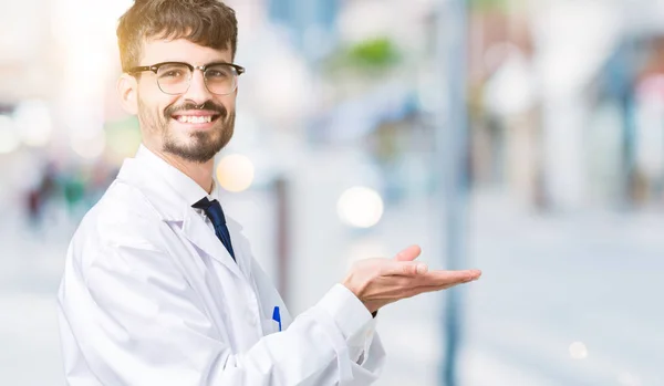 若いプロの科学者男で白衣を着て分離背景手とひら 広告笑顔幸せと自信を持って提示側を指しています — ストック写真