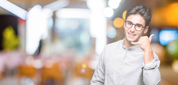 Young handsome man wearing glasses over isolated background smiling doing phone gesture with hand and fingers like talking on the telephone. Communicating concepts.