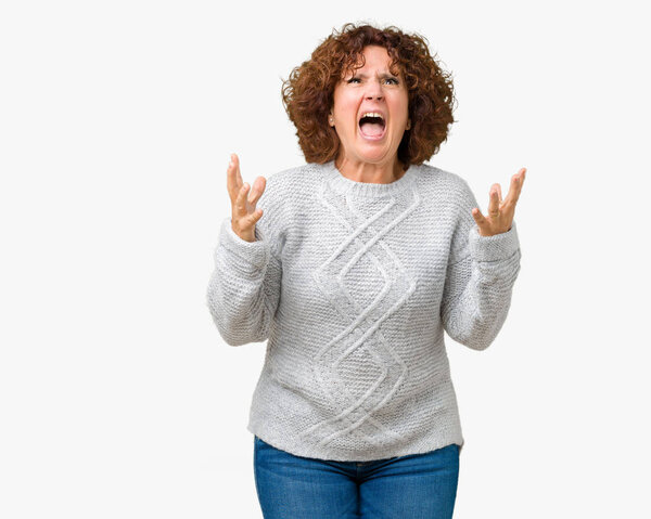 Beautiful middle ager senior woman wearing winter sweater over isolated background crazy and mad shouting and yelling with aggressive expression and arms raised. Frustration concept.