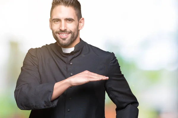 年轻的基督教牧师在孤立的背景示意与手显示大和大的大小标志 措施符号 看着镜头微笑 测量概念 — 图库照片