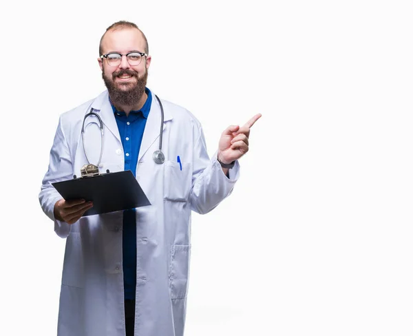 年轻的医生男子拿着剪贴板在孤立的背景指向和显示与愉快的面孔微笑的边 — 图库照片