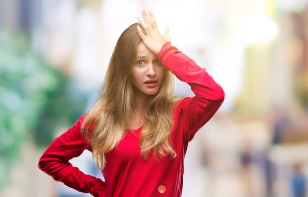 Young beautiful blonde woman wearing red sweater over isolated background surprised with hand on head for mistake, remember error. Forgot, bad memory concept.