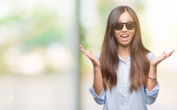 年轻的亚洲妇女戴着太阳镜在孤立的背景下庆祝疯狂和惊讶的成功与手臂举起 睁开眼睛尖叫兴奋 赢家理念 — 图库照片