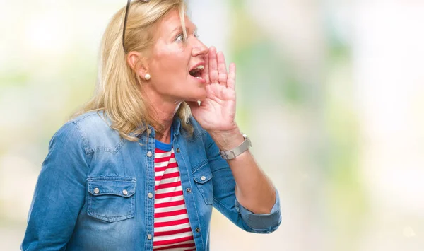 Middle age blonde woman over isolated background shouting and screaming loud to side with hand on mouth. Communication concept.