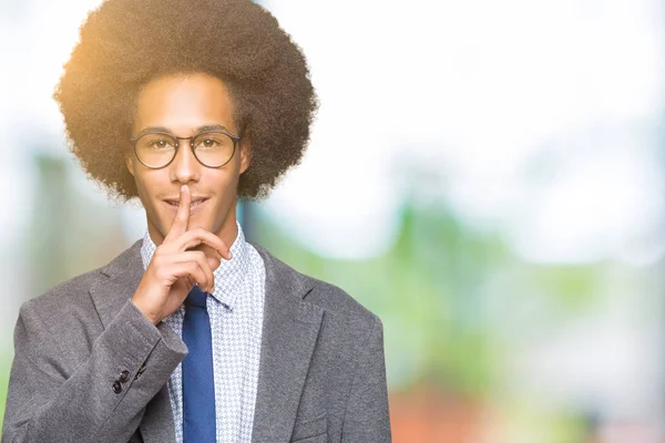 Young african american business man with afro hair wearing glasses asking to be quiet with finger on lips. Silence and secret concept.