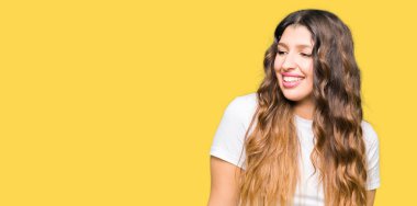 Uzak tarafına yüzünde, doğal ifade gülümseme ile seyir casual beyaz t-shirt giyen genç güzel kadın. Kendine güvenen gülüyor.