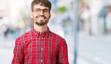 Arka plan eller üzerinde gözlük takan genç yakışıklı adam birlikte izole ve rahat ve neşeli gülümseyen parmak çarpı işareti. Başarı ve iyimser