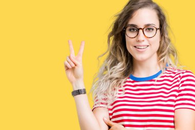 Mutlu yüz zafer işareti yaparken kameraya göz kırpıyor ile gülümseyen izole arka plan üzerinde gözlük güzel sarışın genç kadın. İki numaralı.