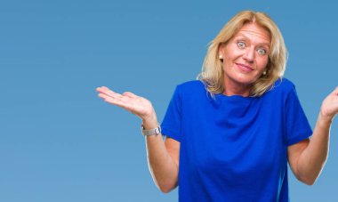 Orta yaş sarışın kadın izole arka plan clueless ve şaşkın bir ifadeyle kollar ve eller kaldırdı. Şüphe kavramı.