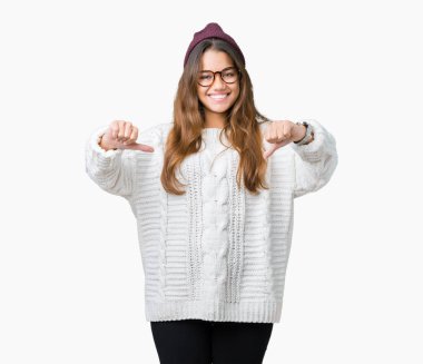 Yüzünde gülümseme ile kendinden emin görünüyorsun, kendini gururlu ve mutlu parmakları ile işaret izole arka plan üzerinde gözlük ve kış şapka giyen genç güzel esmer hipster kadın.