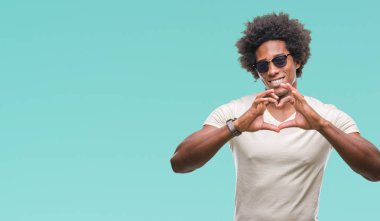 Afro Amerikalı adam aşık kalp simgesi ve elleriyle şekil gösteren gülümseyen izole arka plan üzerinde güneş gözlüğü takıyor. Romantik kavramı.