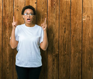 Güzel genç Afro-Amerikan kadın hayrete ve yukarıya bakıyor ve parmakları ile işaret ve silah kaldırdı sürpriz izole arka plan üzerinde gözlük.