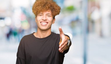 Tebrik ve konuksever dost sunan karşılıklı gülümseyen siyah t-shirt giyen afro saçlı Genç yakışıklı adam. Başarılı iş.