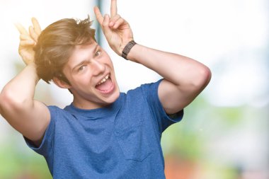 Neşeli gülümseyen izole arka plan tavşan kulakları, komik ve çılgın baş parmaklar ile poz üzerinde mavi t-shirt giyen genç yakışıklı adam