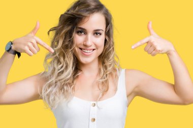 Yüzünde gülümseme ile kendinden emin görünüyorsun, kendini gururlu ve mutlu parmakları ile işaret izole arka plan genç güzel sarışın kadın.