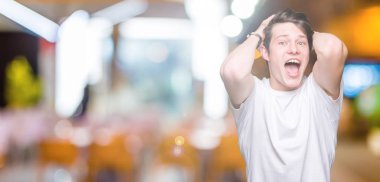 T-shirt üzerinde arka plan deli izole ve ile korkuttu casual beyaz giyen genç yakışıklı adam kafasına, korkmuş ve şaşırmış şok açık ağız ile eller