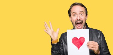 Kocaman bir gülümseme ile çığlık ve ellerini kaldırdı zaferini kutluyor kırmızı kalp çok mutlu ve heyecanlı, kazanan ifade ile kağıt tutan yakışıklı orta yaş erkek