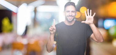 Yakışıklı delikanlı gösterilen ve parmakları ile işaret izole arka plan üzerinde kendinden emin ve mutlu gülümseyerek süre 6 numara.