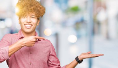 Hayret ve el ile sunulması ve parmak ile işaret ederken kameraya gülümseyen afro saçlı Genç yakışıklı iş adamı.