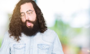 Uzun saç ve sakal giyen genç hipster adamla dudaklı, çılgın ve komik bir jest yapma balık yüz gözlük. Komik ifade.