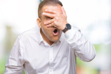 Mahcup ifadeyle parmaklarımın arasından görünen orta yaş Arap zarif adam yüz ve gözler el ile kapsayan şok bakmak izole arka plan üzerinde.