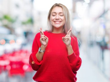 Umut ve gözleri kapalı geçiş parmaklarıyla gülümseyen izole arka plan üzerinde kış kazak giyen genç sarışın kadın. Şans ve batıl kavramı.