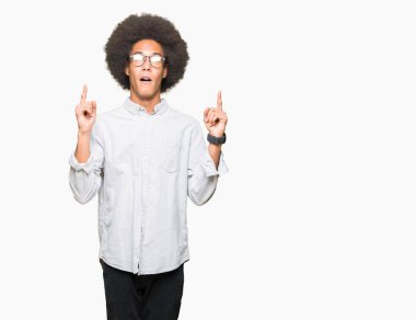 Afro saçlı gözlüklü genç Afro-Amerikan adam hayret ve yukarıya bakıyor ve parmakları ile işaret ve silah kaldırdı şaşırttı.