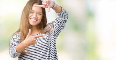 Elle yapma çerçeve ve parmakları ile mutlu yüz gülümseyen izole arka plan üzerinde çizgili süveter giyen genç güzel esmer kadın. Yaratıcılık ve Fotoğrafçılık kavramı.