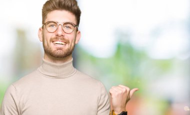 Seyir ve başparmak yanında yukarıyı mutlu yüz ile gülümseyen gözlüklü genç yakışıklı iş adamı.