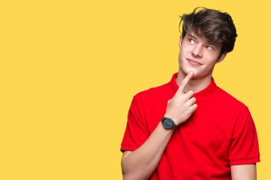 Çene düşünme hakkında soru, dalgın ifade üzerine el ile izole arka plan üzerinde kırmızı t-shirt giyen genç yakışıklı adam. Düşünceli yüzüyle gülümsüyor. Şüphe kavramı.