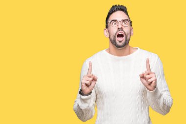 Yakışıklı delikanlı hayrete ve yukarıya bakıyor ve parmakları ile işaret ve silah kaldırdı sürpriz izole arka plan üzerinde gözlük.