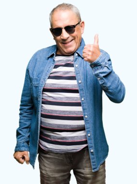 Denim ceket ve hareketi el ile mutlu yaşasın yaparken güneş gözlüğü takan yakışıklı komuta sizde. Kameraya bakarak başarı gösteren ile ifade onaylama.