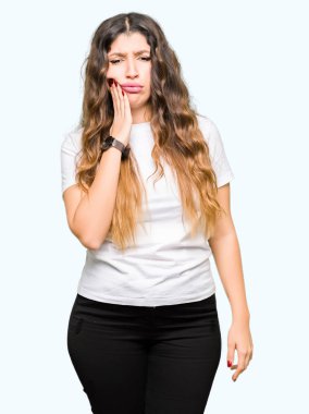 Genç güzel kadın diş ağrısı veya diş üzerinde diş hastalığı nedeniyle ağrılı ifade ile el ile ağız dokunmadan rahat beyaz t-shirt giyiyor. Diş hekimi konsepti.