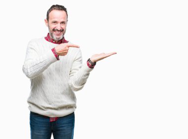 Orta yaş ağarmış komuta sizde hayrete ve el ile sunulması ve parmak ile işaret ederken kameraya gülümseyen izole arka plan üzerinde kış kazak giyiyor.