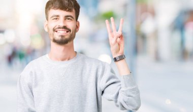 Gösterilen arka plan üzerinde sweatshirt giyen genç yakışıklı adam izole ve parmakları ile işaret üçüncü gülümseyen ise kendinden emin ve mutlu.