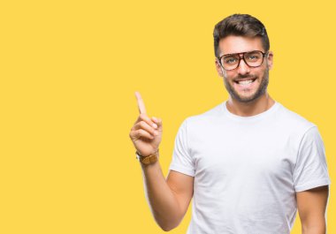 Kameraya bakarak yan el ve parmak ile işaret yüzünde kocaman bir gülümseme ile izole arka plan üzerinde gözlük takan genç yakışıklı adam.