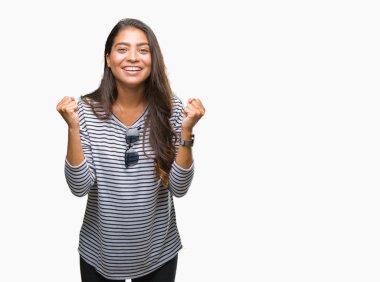 Genç güzel Arap kadın izole arka plan kutlama üzerinde güneş gözlüğü takıyor şaşırttı ve başarı için kaldırdı kollarını açarak hayret ve gözleri açık. Kazanan kavramı.