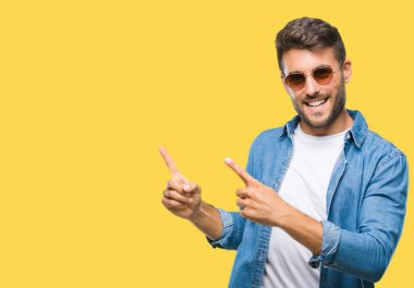 Yakışıklı delikanlı gülümseyen ve iki elleri ve parmakları ile tarafına işaret kamera bakarak izole arka plan üzerinde güneş gözlüğü takıyor.