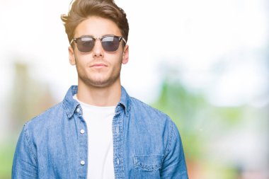 Yakışıklı delikanlı üzerinde güneş gözlüğü takıyor arka plan gevşek yüzünde ciddi bir ifade ile izole. Basit ve doğal kameraya bakıyor.