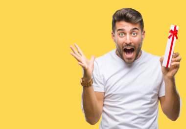 Sevgililer günü hediyesi üzerinde kocaman bir gülümseme ile çığlık zaferini kutluyor ve ellerini kaldırdı izole arka plan çok mutlu ve heyecanlı, kazanan ifade veren aşık genç yakışıklı adam