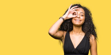 Kıvırcık saçlı gülümseyerek el parmakları ile mutlu yüz üzerinden seyir göz ile ok jest yapmak moda etek giyen genç güzel kız.