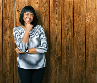 Giyen güzel genç Afro-Amerikan kadın kazak emin çapraz kollar ve çeneme kaldırdı el ile gülümseme ile kameraya bakarak izole arka plan üzerinde çizgili. Pozitif düşünce.