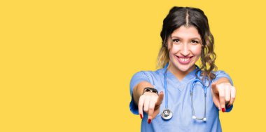 Olumlu ve neşeli gülümseyen Tıbbi üniforma işaretleme ve parmaklar, kamerayla giyen genç yetişkin doktor kadın