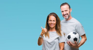 Orta yaş İspanyol çift işaret ve başparmak kadar mutlu yüz gülümseyen tarafı ile gösteren izole arka plan üzerinde futbol futbol topu tutan