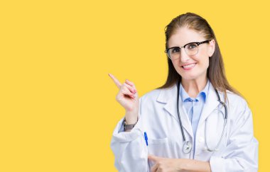Kameraya bakarak yan el ve parmak ile işaret yüzünde kocaman bir gülümseme ile izole arka plan üzerinde tıbbi ceket giyen orta yaş olgun doktor kadın.