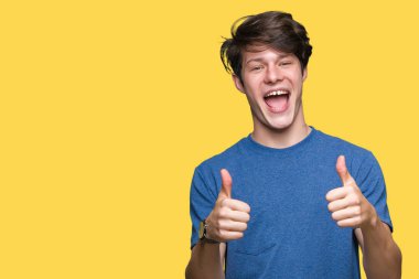 Yakışıklı delikanlı üzerinde el ile pozitif jest yapıyor izole arka plan başarı işareti mavi t-shirt giyen başparmak gülümseyen ve mutlu. Neşeli bir ifadeyle, kazanan jest kameraya bakıyor.