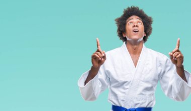 Afro Amerikalı adam izole arka plan üzerinde karate kimono giyen hayrete ve yukarıya bakıyor ve parmakları ile işaret ve silah kaldırdı şaşırttı.