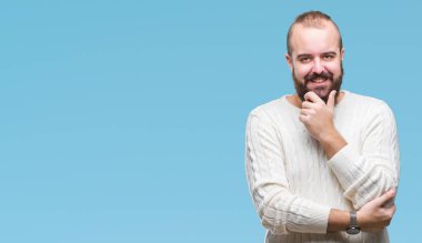 Emin çapraz kollar ve çeneme kaldırdı el ile gülümseme ile kameraya bakarak izole arka plan üzerinde kış kazak giyen genç beyaz hipster adam. Pozitif düşünce.